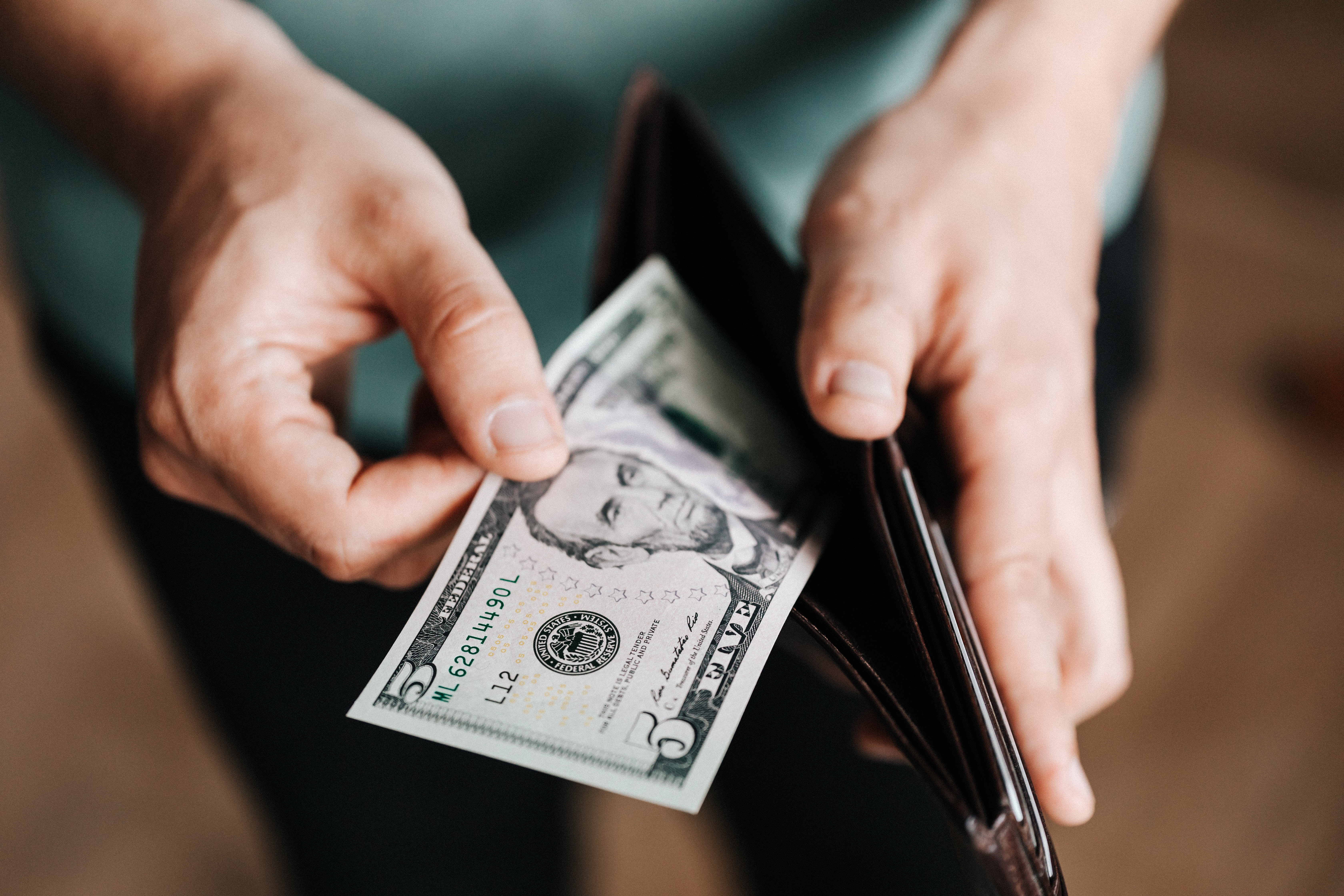 a man opening up his wallet to reveal a five dollar bill